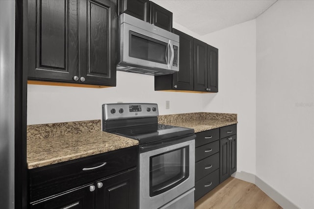 kitchen with light wood-type flooring, stone counters, and appliances with stainless steel finishes