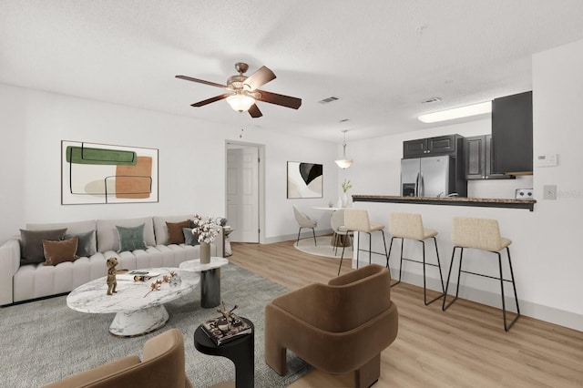 living room with baseboards, visible vents, a ceiling fan, a textured ceiling, and light wood-type flooring