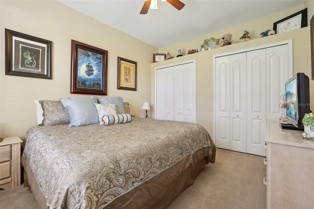 bedroom with ceiling fan, light carpet, and two closets