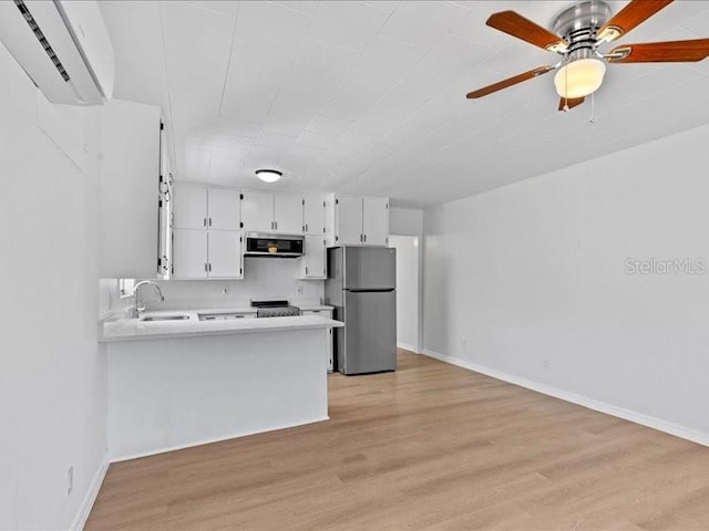 kitchen featuring a wall mounted air conditioner, ventilation hood, white cabinetry, sink, and stainless steel fridge