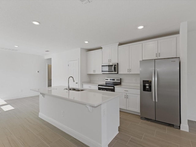 kitchen with sink, a breakfast bar, white cabinetry, stainless steel appliances, and a center island with sink