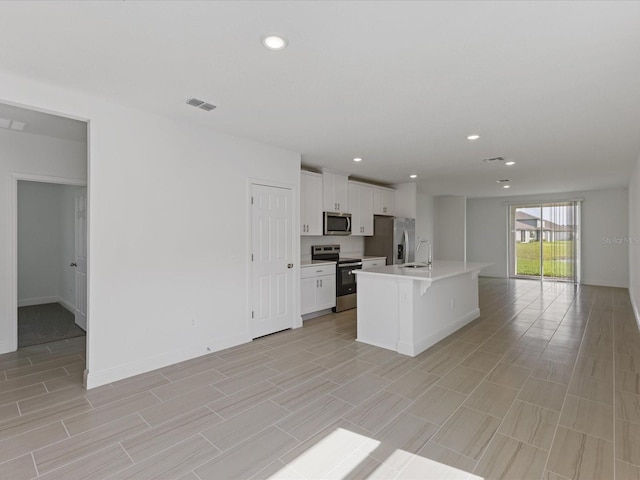 kitchen featuring appliances with stainless steel finishes, white cabinetry, sink, a kitchen breakfast bar, and a center island with sink