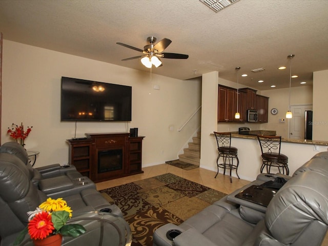 living room with light tile patterned flooring, ceiling fan, a textured ceiling, and a fireplace