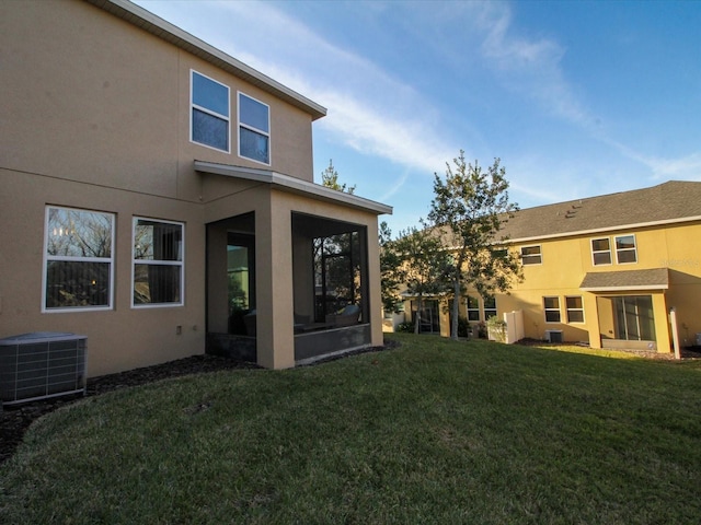 back of house featuring central AC unit, a lawn, a sunroom, and stucco siding