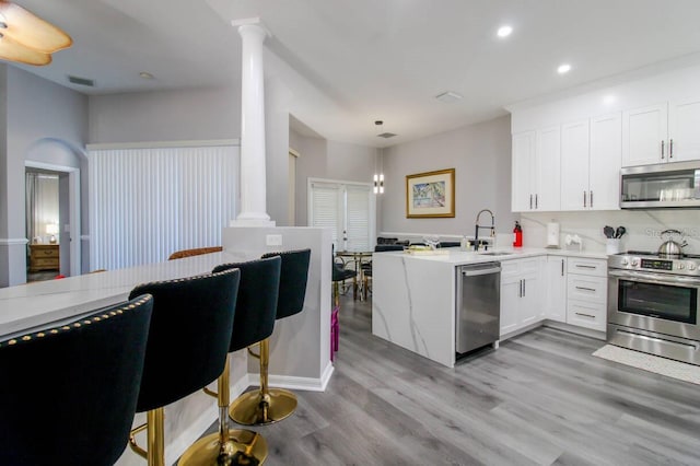 kitchen with ornate columns, appliances with stainless steel finishes, white cabinets, and kitchen peninsula