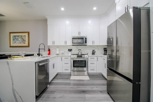 kitchen featuring sink, stainless steel appliances, light hardwood / wood-style floors, white cabinets, and kitchen peninsula