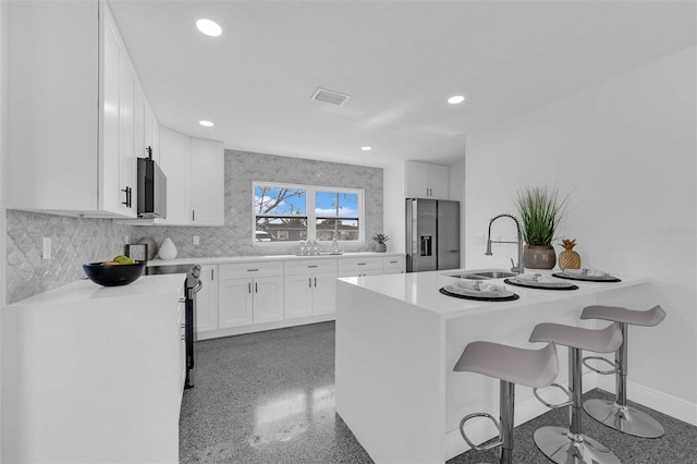 kitchen with a breakfast bar, white cabinetry, sink, stainless steel fridge, and decorative backsplash