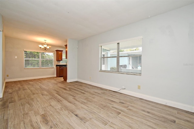 unfurnished living room with lofted ceiling, plenty of natural light, a chandelier, and light hardwood / wood-style flooring