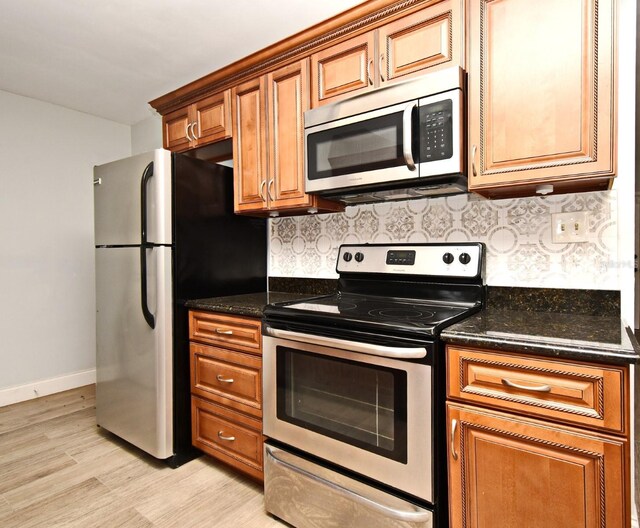 kitchen featuring decorative backsplash, stainless steel appliances, dark stone counters, and light wood-type flooring