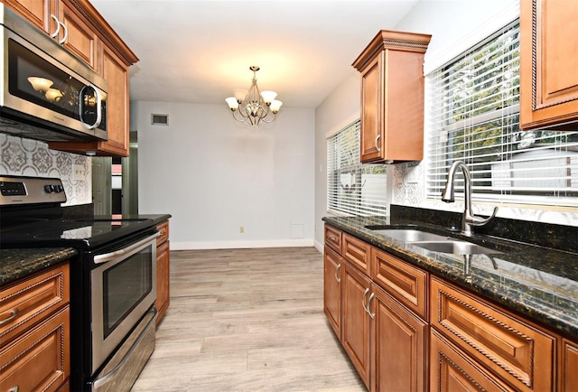 kitchen with appliances with stainless steel finishes, decorative light fixtures, sink, dark stone counters, and light wood-type flooring