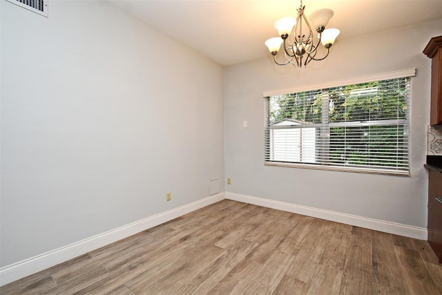 spare room featuring an inviting chandelier and light hardwood / wood-style floors