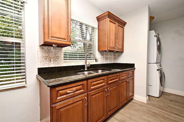 kitchen with dark stone countertops, sink, decorative backsplash, and stacked washing maching and dryer