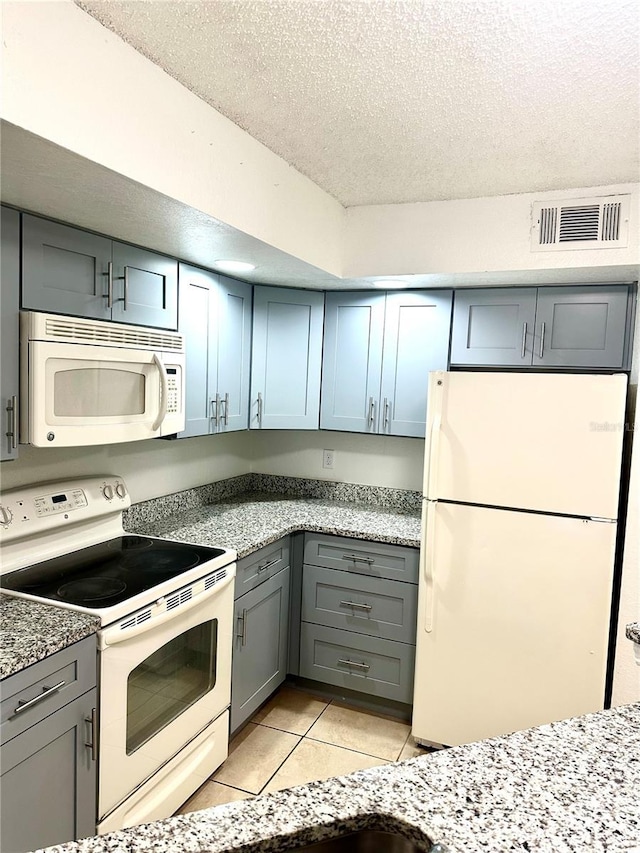 kitchen with light tile patterned floors, white appliances, gray cabinetry, light stone countertops, and a textured ceiling