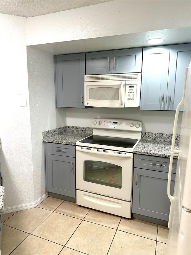 kitchen featuring gray cabinetry, light tile patterned floors, white appliances, and stone counters