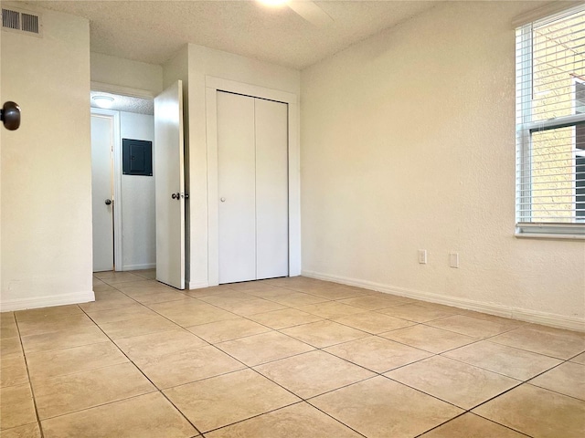 unfurnished bedroom with light tile patterned flooring, a textured ceiling, electric panel, a closet, and ceiling fan