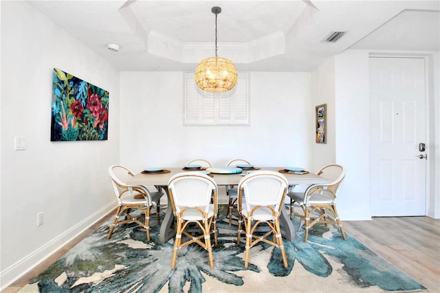 dining space with wood-type flooring, ornamental molding, and a raised ceiling