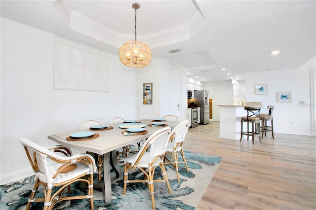 dining area featuring crown molding, a notable chandelier, light wood-type flooring, and a tray ceiling