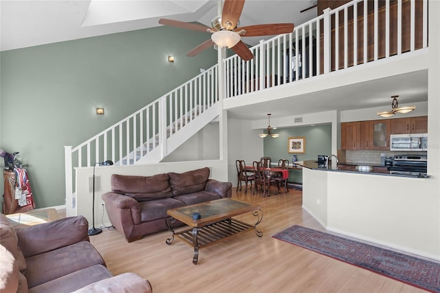 living room featuring ceiling fan, light hardwood / wood-style floors, and a high ceiling