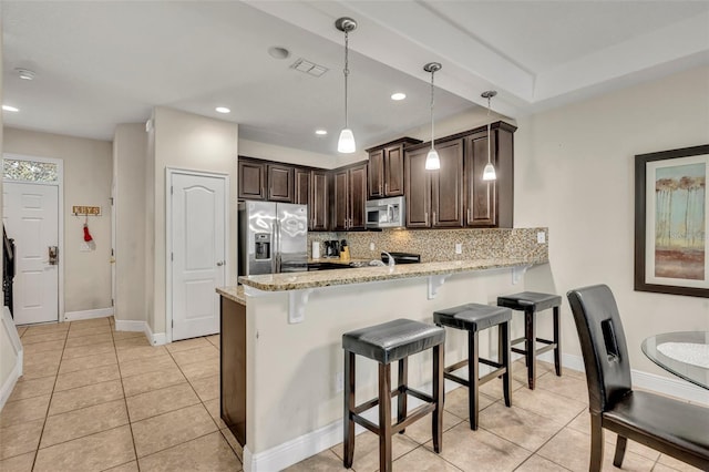 kitchen featuring appliances with stainless steel finishes, pendant lighting, tasteful backsplash, light stone counters, and kitchen peninsula