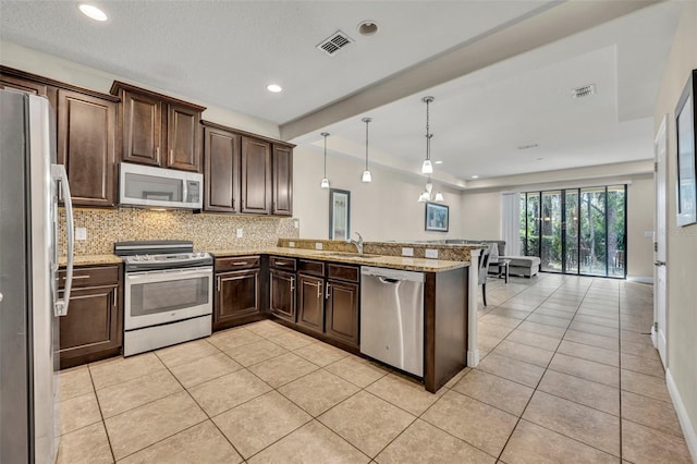 kitchen with light tile patterned flooring, decorative light fixtures, appliances with stainless steel finishes, kitchen peninsula, and light stone countertops