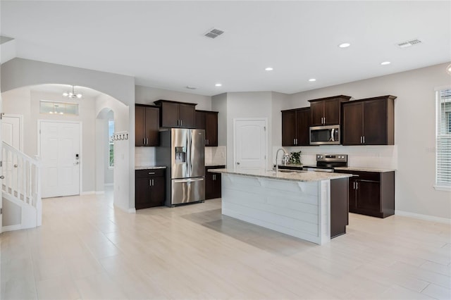 kitchen with a kitchen island with sink, light stone countertops, dark brown cabinets, and stainless steel appliances