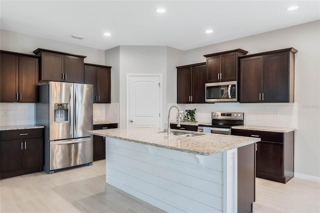 kitchen featuring sink, dark brown cabinets, a center island with sink, appliances with stainless steel finishes, and light stone countertops