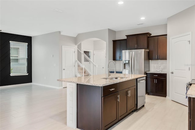 kitchen featuring dark brown cabinetry, sink, appliances with stainless steel finishes, light stone countertops, and a kitchen island with sink