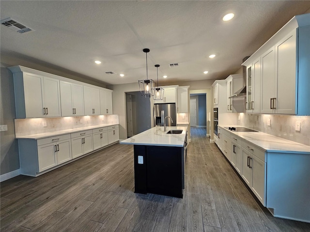 kitchen featuring stainless steel fridge, dark hardwood / wood-style flooring, pendant lighting, a kitchen island with sink, and white cabinets