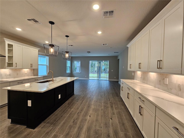 kitchen with sink, decorative light fixtures, a kitchen island with sink, decorative backsplash, and white cabinets