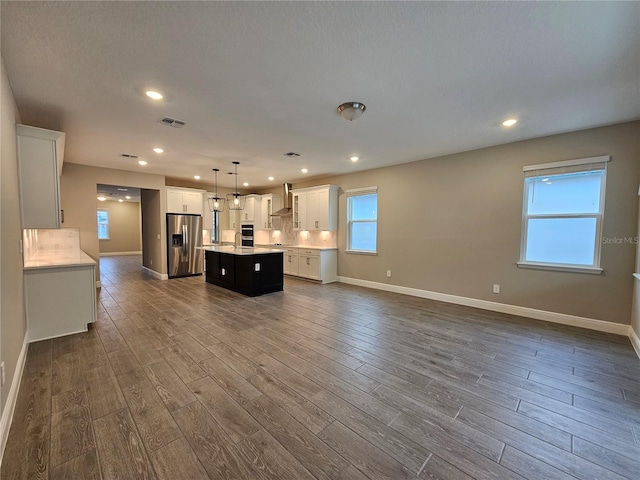 kitchen with wall chimney exhaust hood, a center island, dark hardwood / wood-style floors, stainless steel fridge, and pendant lighting