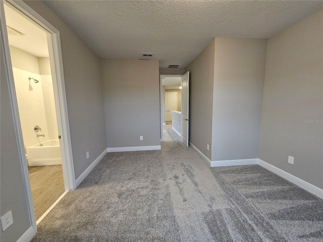 unfurnished bedroom with light carpet, connected bathroom, and a textured ceiling