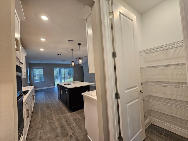 kitchen featuring white cabinetry, sink, pendant lighting, and an island with sink