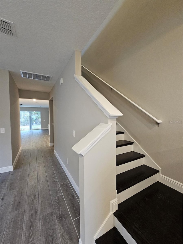 stairs with hardwood / wood-style floors and a textured ceiling