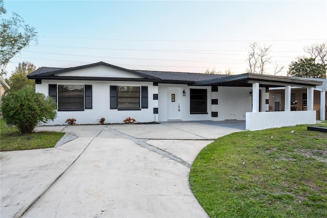 view of front of property featuring stucco siding, an attached carport, a front lawn, and driveway