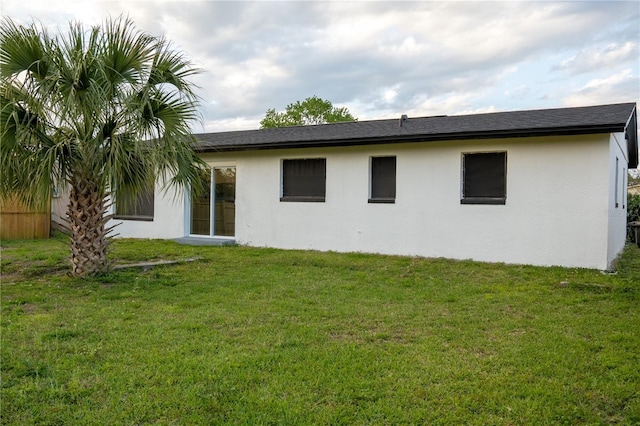 rear view of house with stucco siding and a lawn