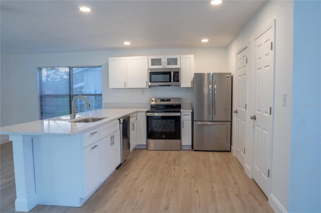 kitchen with a peninsula, a sink, appliances with stainless steel finishes, white cabinetry, and light wood-type flooring