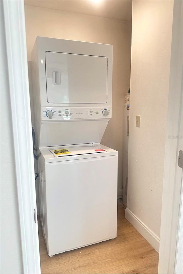 clothes washing area featuring laundry area, light wood-style flooring, baseboards, and stacked washer / drying machine