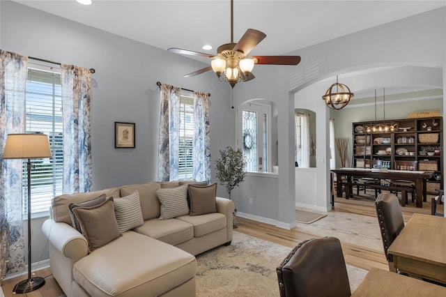 living room featuring a healthy amount of sunlight, ceiling fan with notable chandelier, and light hardwood / wood-style floors