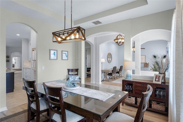 dining area with an inviting chandelier, a raised ceiling, and light wood-type flooring