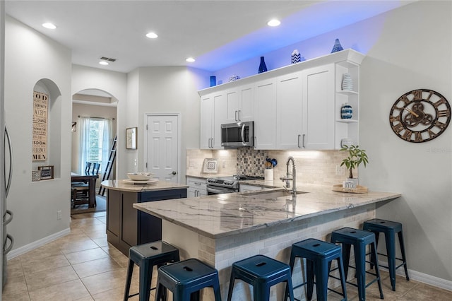 kitchen with a breakfast bar, white cabinetry, stainless steel appliances, light stone counters, and kitchen peninsula