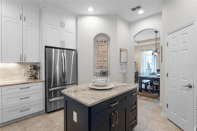 kitchen with white cabinetry, decorative light fixtures, stainless steel refrigerator, and a kitchen island