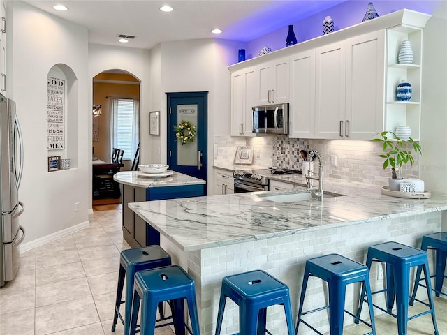 kitchen with a breakfast bar, white cabinetry, light stone counters, kitchen peninsula, and stainless steel appliances