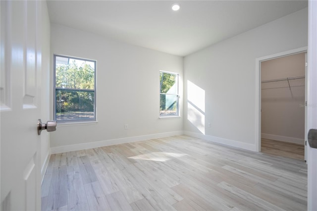 unfurnished bedroom with multiple windows, a spacious closet, light hardwood / wood-style floors, and a closet