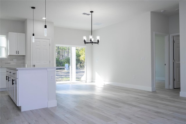 kitchen featuring decorative light fixtures, white cabinets, decorative backsplash, a high ceiling, and light hardwood / wood-style flooring