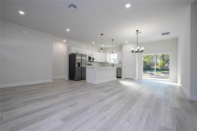 kitchen with light hardwood / wood-style flooring, appliances with stainless steel finishes, a kitchen island, pendant lighting, and white cabinets