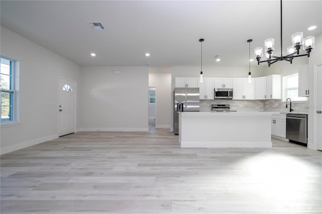 kitchen with appliances with stainless steel finishes, white cabinetry, hanging light fixtures, a center island, and light hardwood / wood-style floors