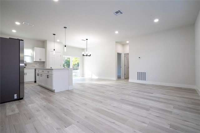 kitchen featuring pendant lighting, white cabinets, stainless steel fridge, backsplash, and a center island