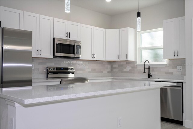 kitchen featuring sink, white cabinetry, pendant lighting, stainless steel appliances, and light stone countertops