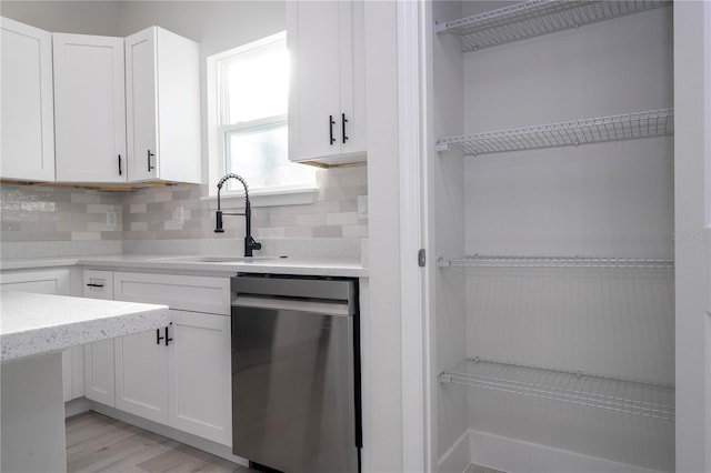 kitchen featuring sink, stainless steel dishwasher, white cabinets, light hardwood / wood-style floors, and backsplash