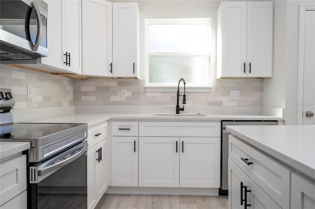 kitchen with sink, white cabinetry, backsplash, stainless steel appliances, and light stone counters